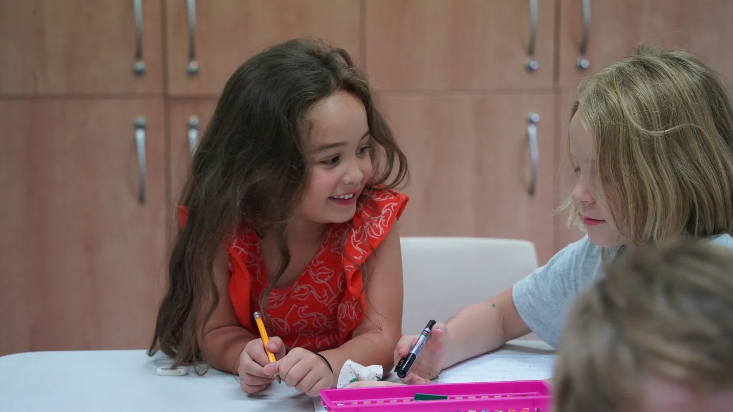 Two girls smiling as they draw together at a craft table at Children’s Church, CoastWIDE Church