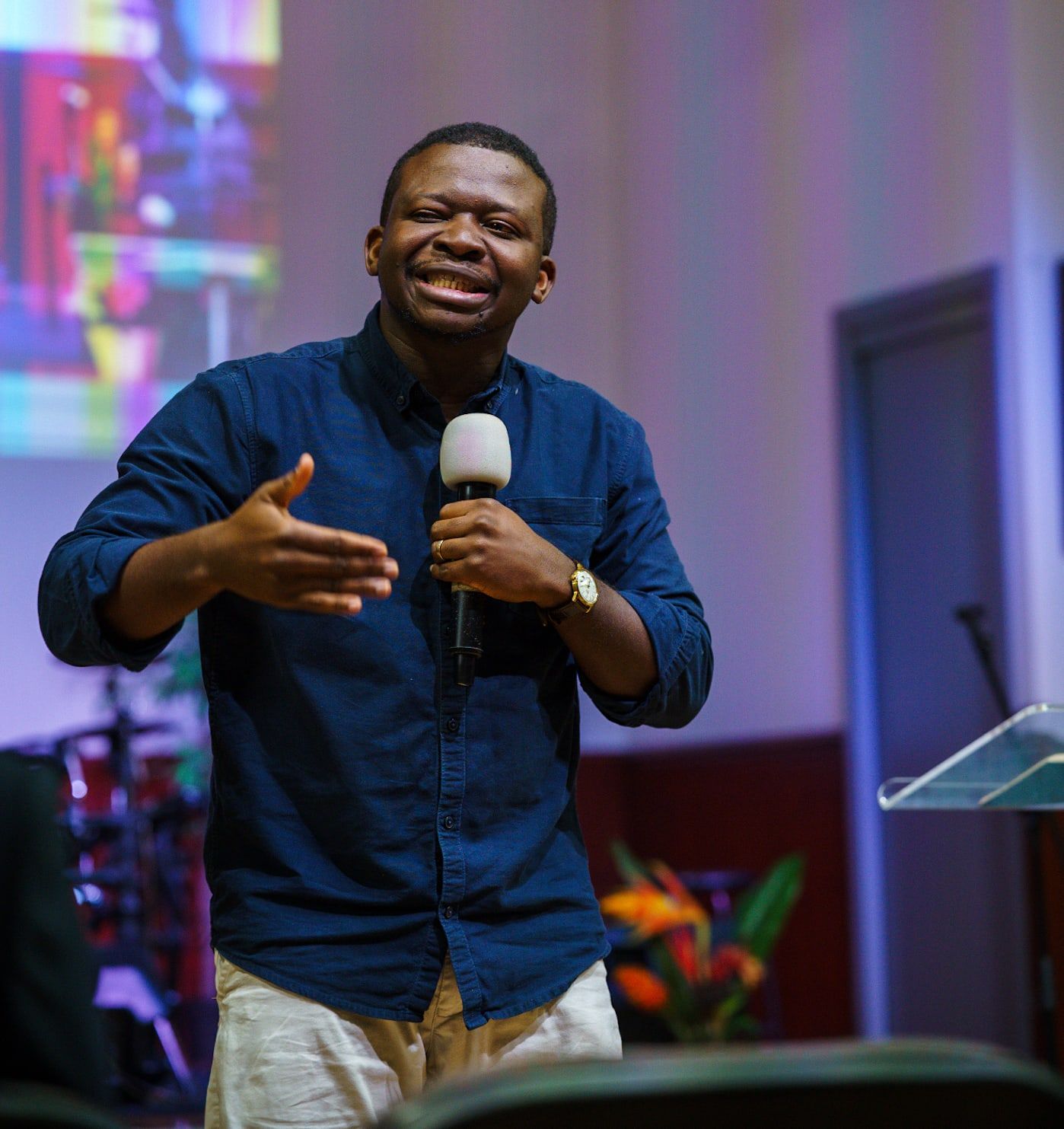Young Adults Leader Delight Madujibeya smiling and speaking with a microphone, wearing a denim shirt