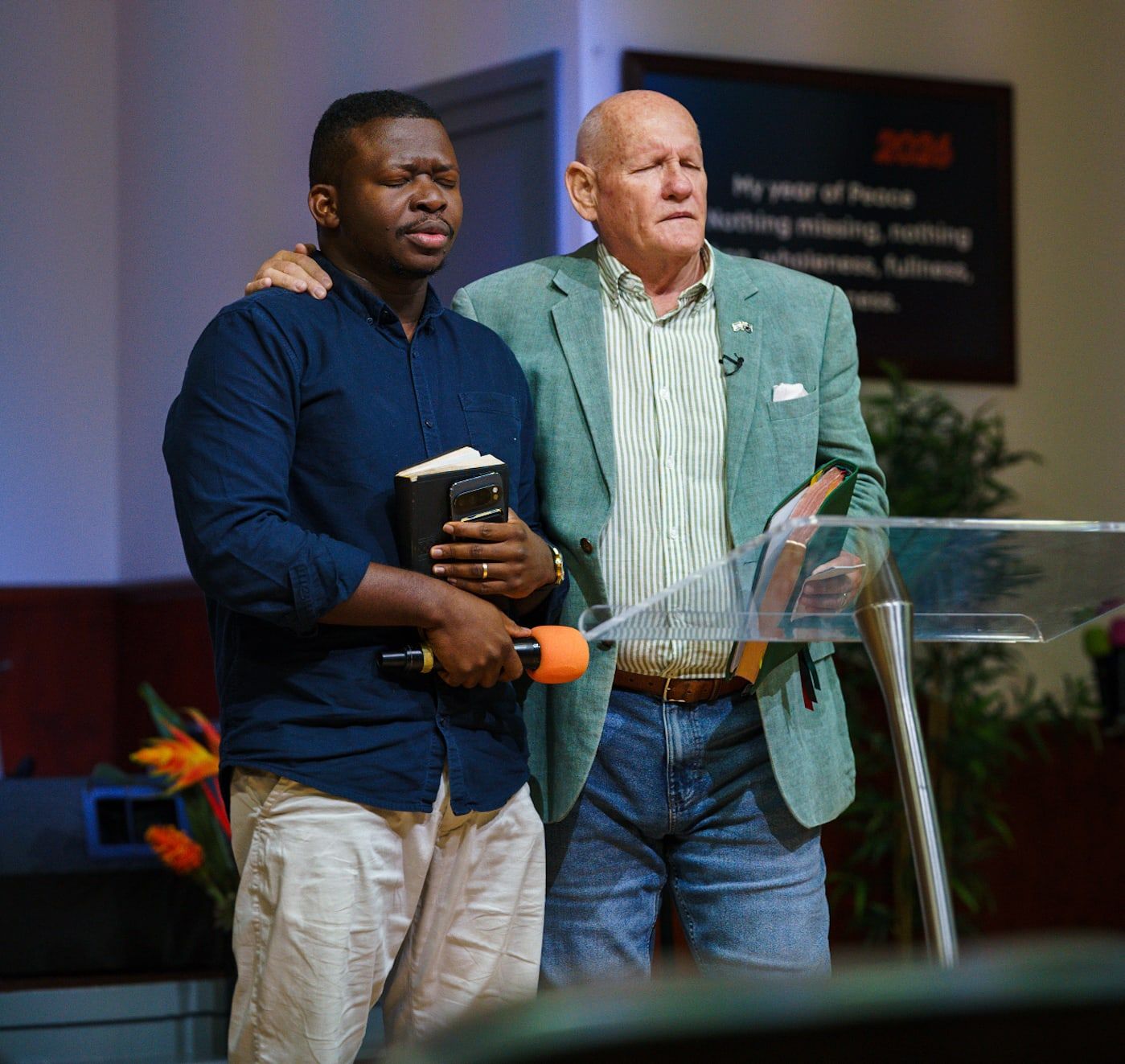 Pastor Shayne with his arm around a young man holding a Bible and a microphone, praying