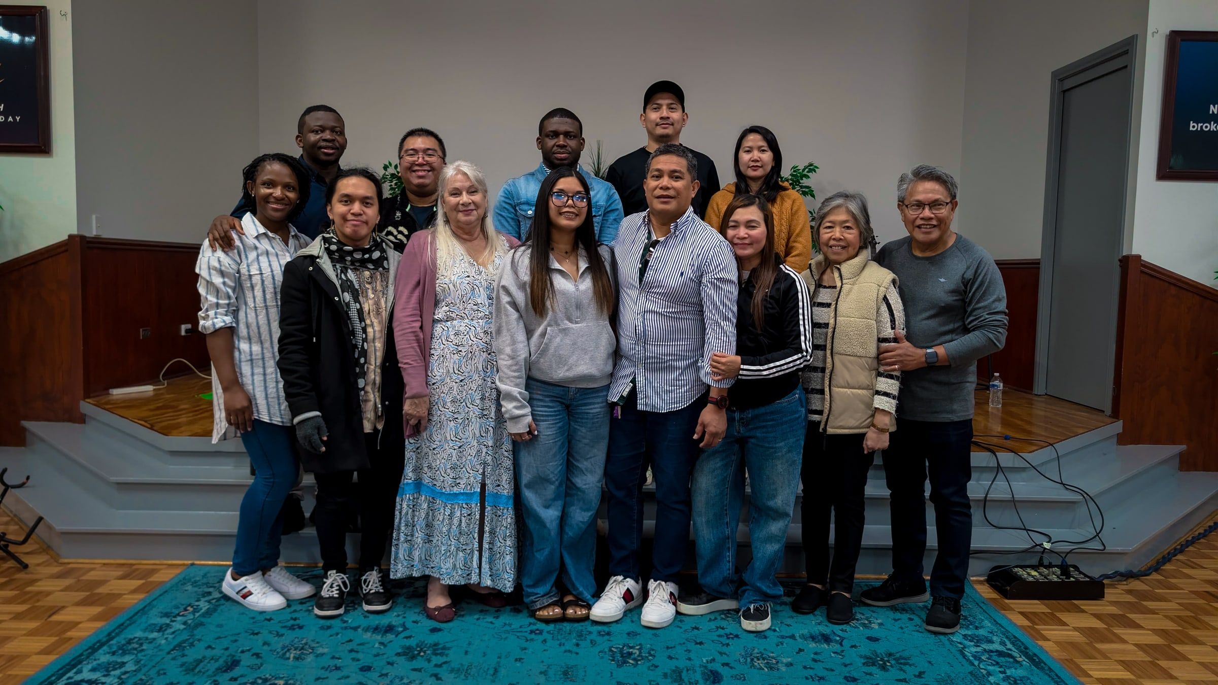 The CoastWIDE Church worship team, about a dozen men and women of many cultural backgrounds, standing together and smiling on the stage steps in Arundel, Gold Coast