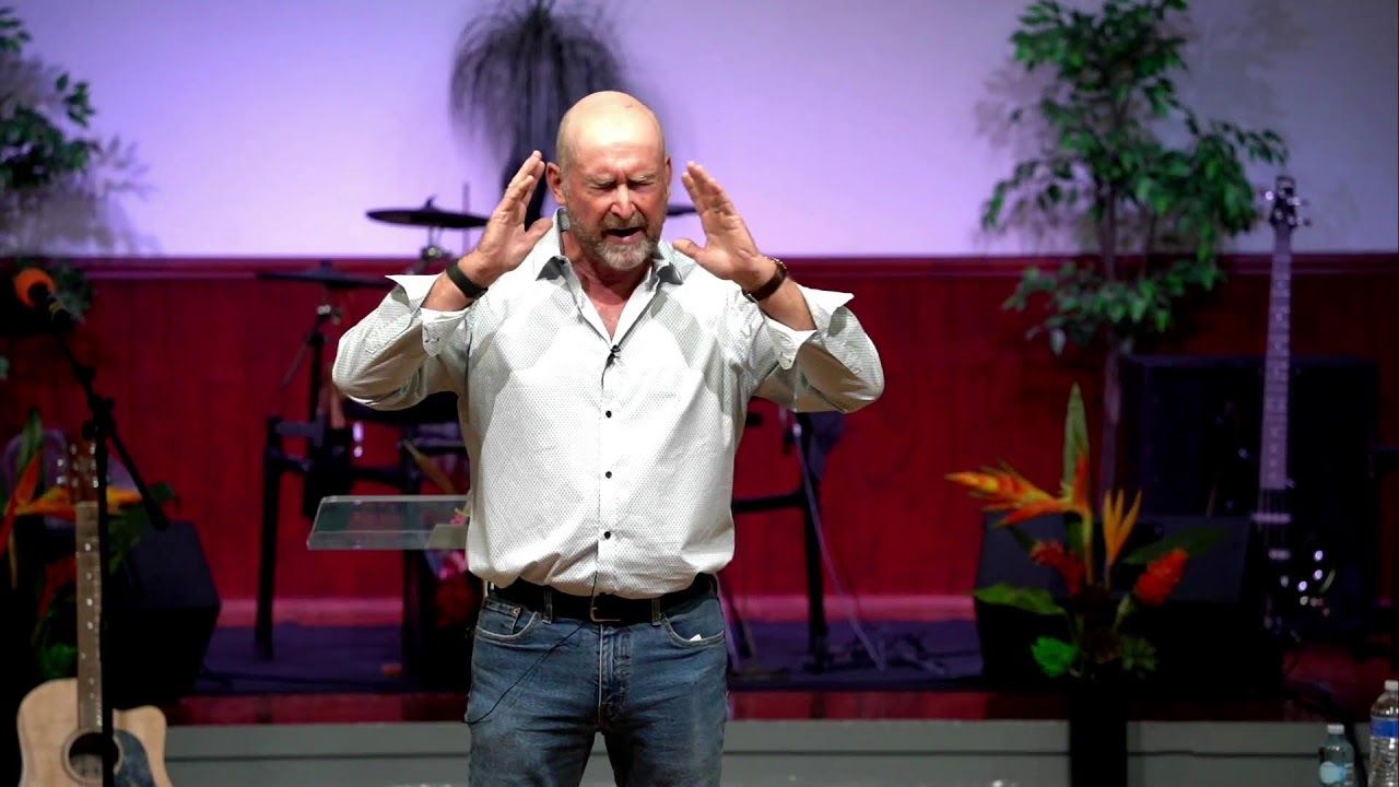 A speaker preaching with both hands raised on stage at CoastWIDE Church, Gold Coast