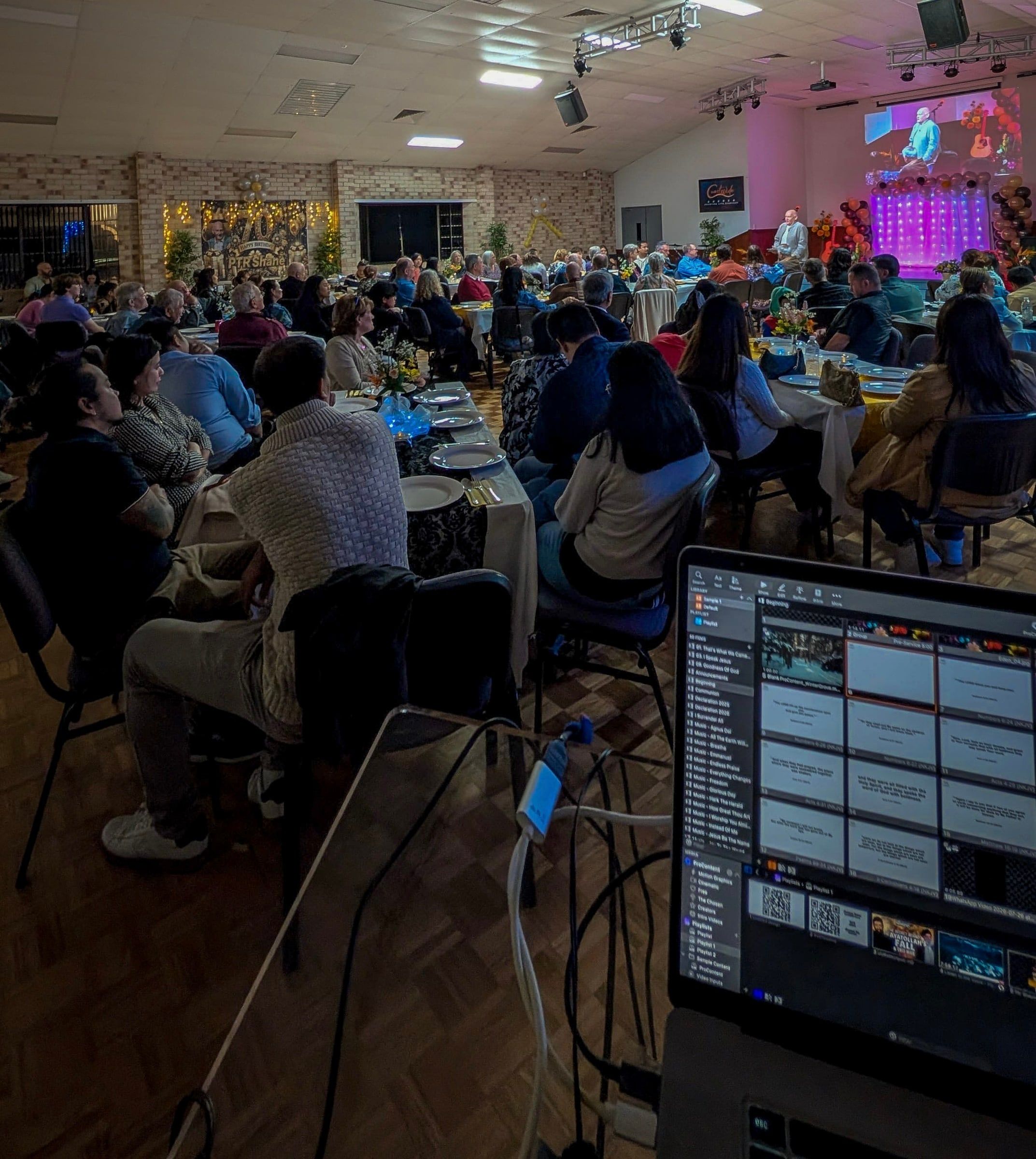 The packed hall at CoastWIDE Church, Gold Coast, seen from the back as people sit together at tables during a church gathering