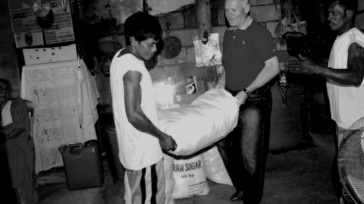 CoastWIDE Church missions: Pastor Shayne Cunningham hands out sacks of raw sugar as relief aid alongside local men, in black and white