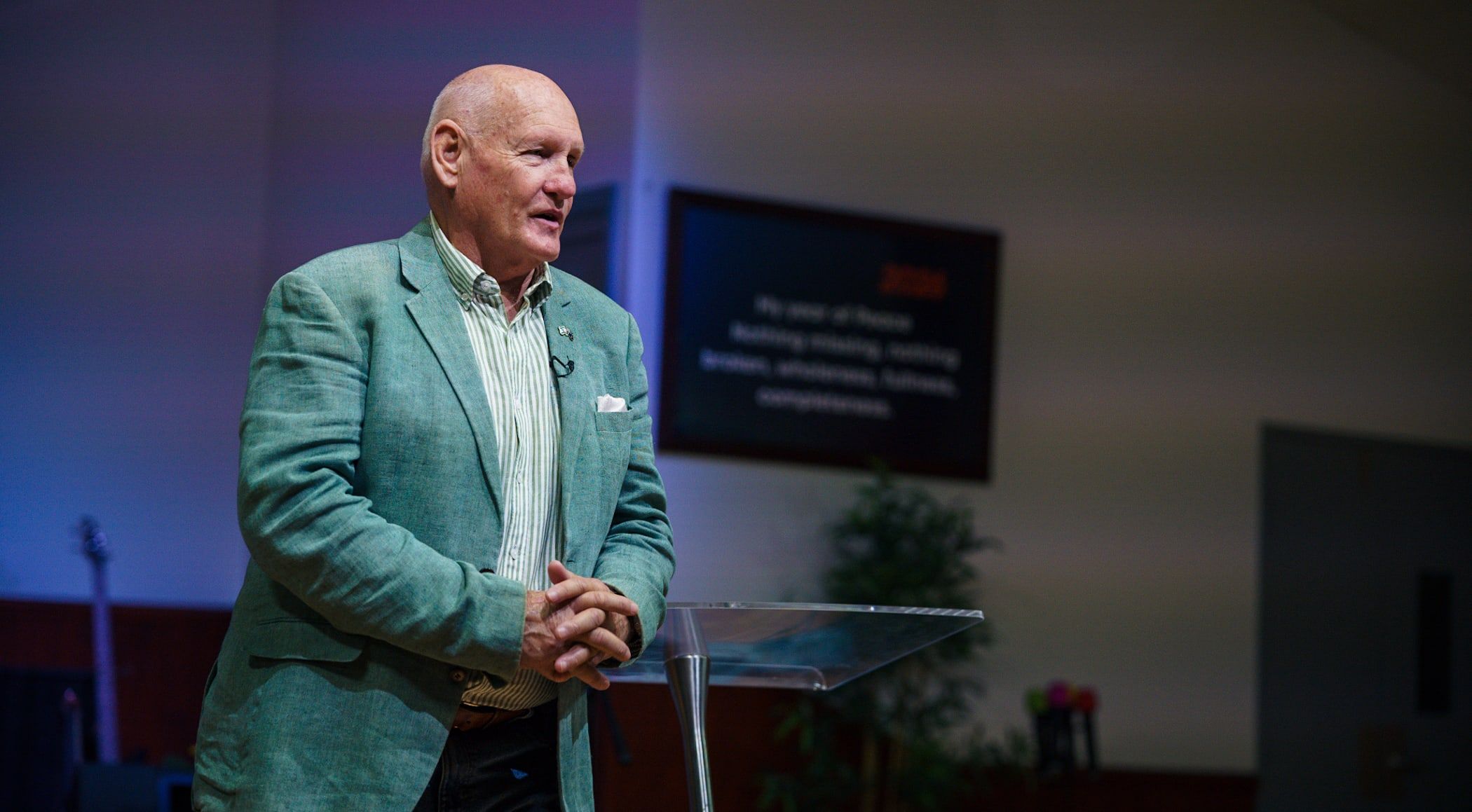 Pastor Shayne Cunningham speaking at the lectern in a green jacket