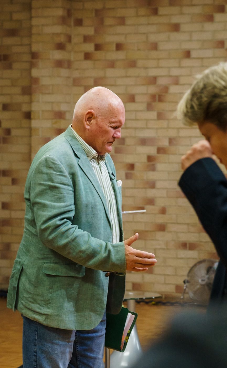 Pastor Shayne Cunningham praying with his hand outstretched in front of a brick wall