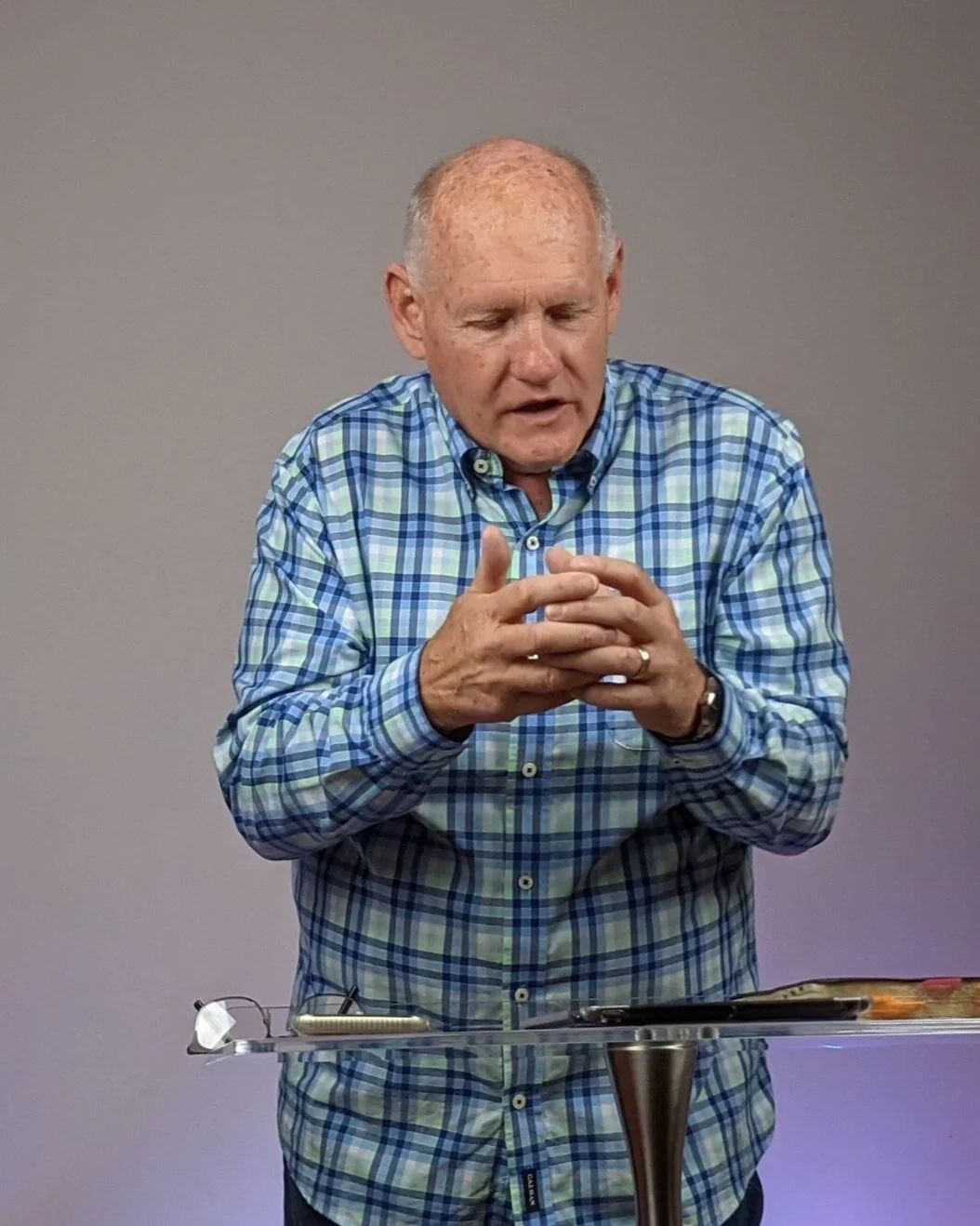 Pastor Shayne Cunningham, Senior Pastor of CoastWIDE Church, speaking at a glass lectern with his hands clasped