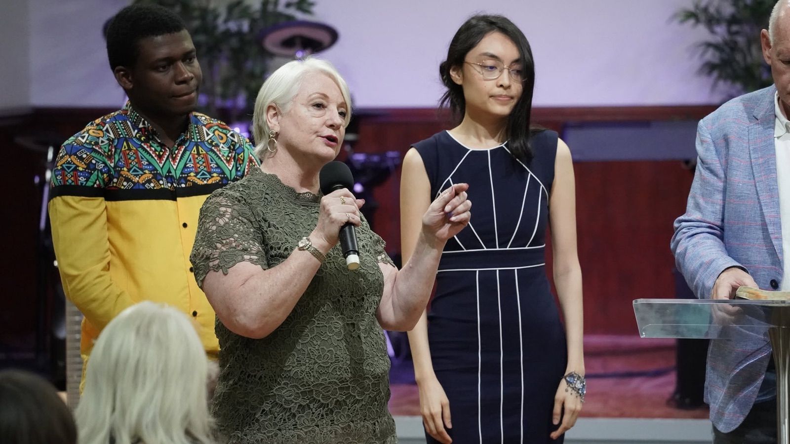 Pastor Susan Cunningham speaking with a microphone, two young people standing beside her