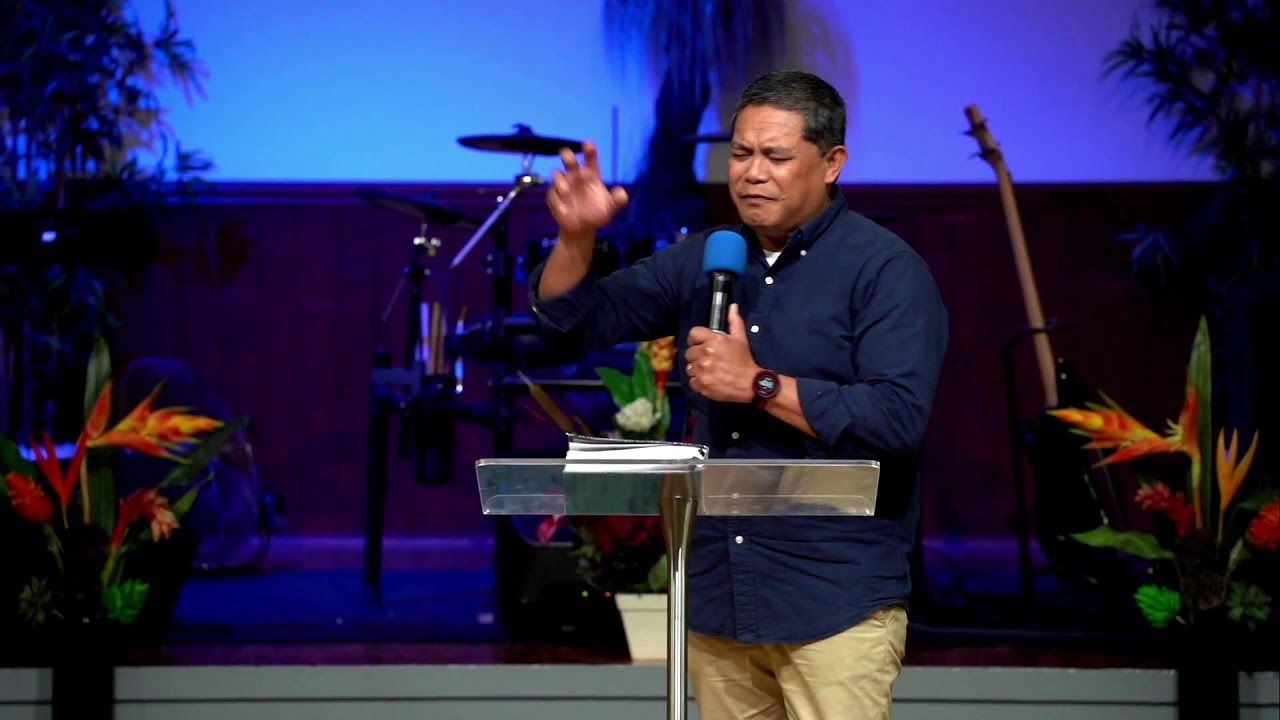 A speaker preaching with a microphone under blue stage lights at CoastWIDE Church
