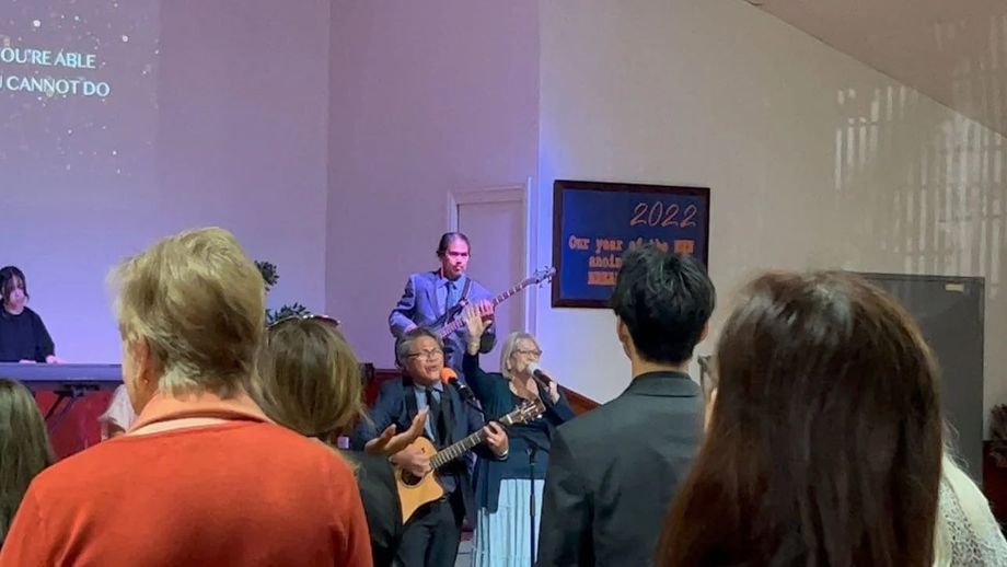 The band leads worship under purple light at CoastWIDE Church, the congregation standing with lyrics on screen