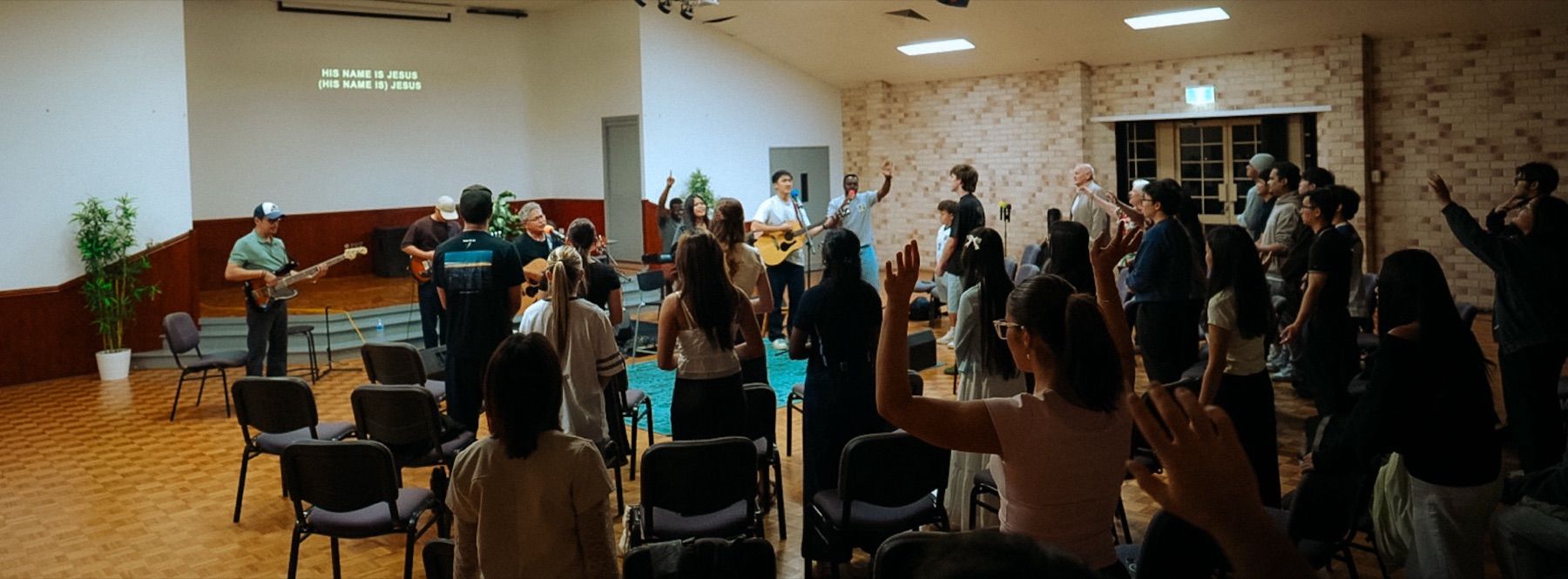 A hall full of young people worshipping with hands raised as the band leads at CoastWIDE Church, Arundel